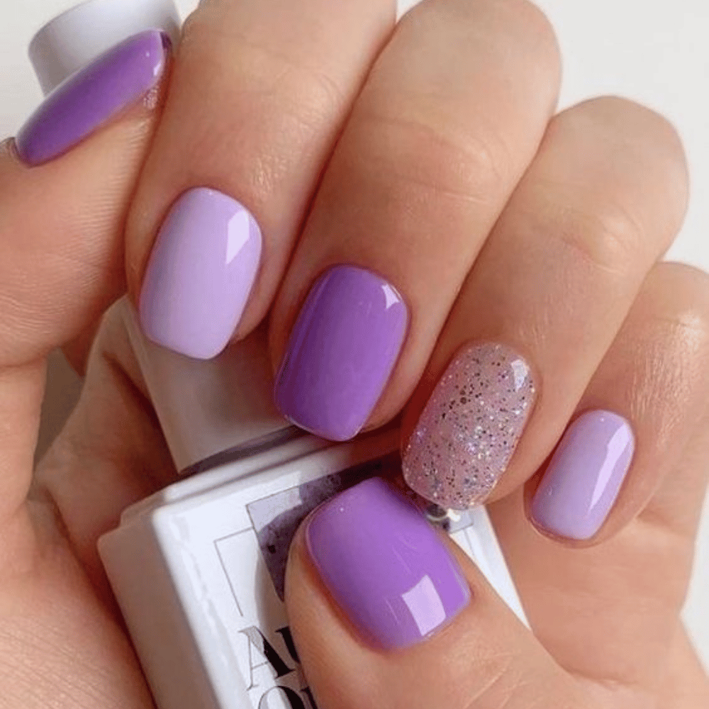 A hand with long nails in various shades of purple, holding a white nail polish bottle.