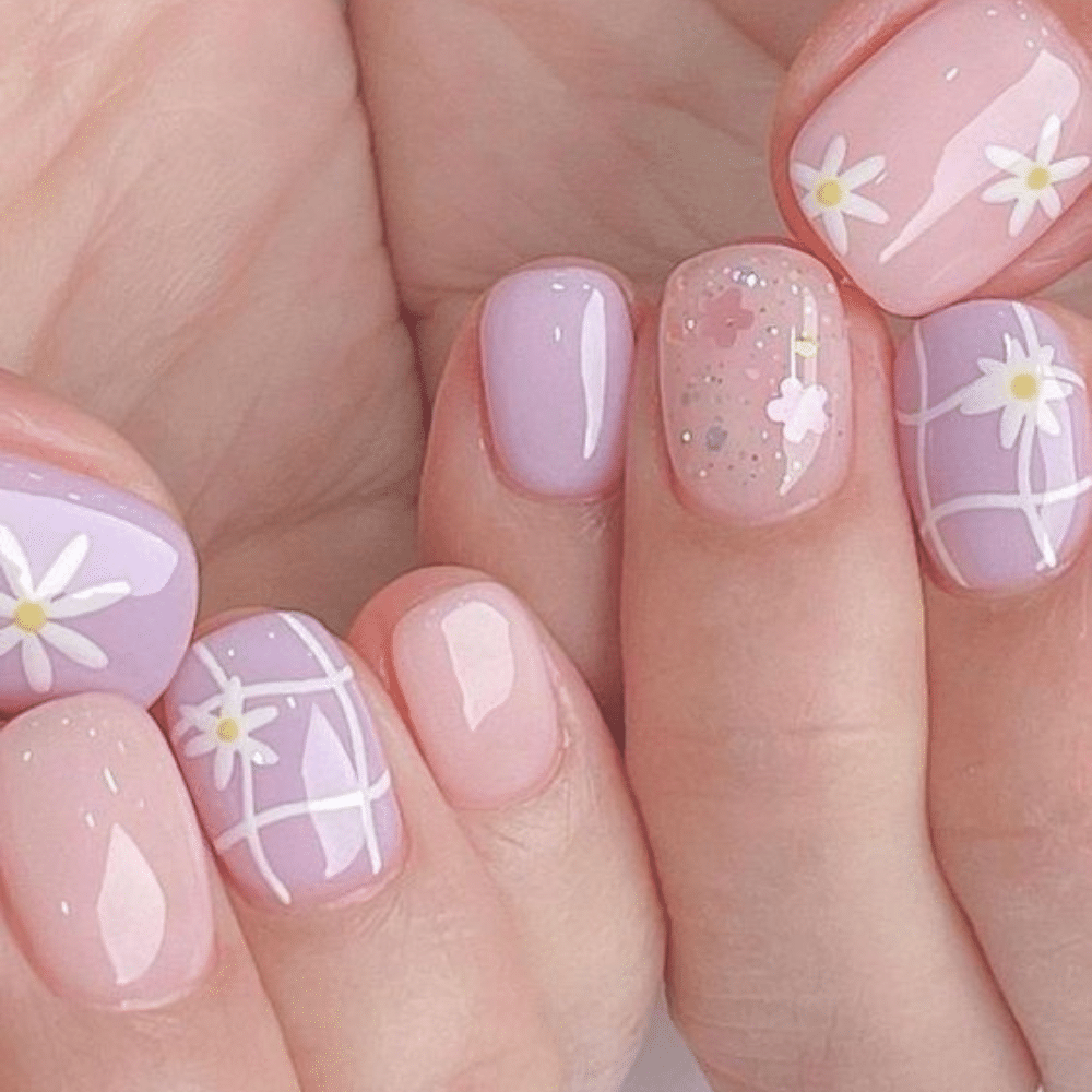 Close-up of hands with pastel pink and purple nails, featuring floral and grid designs.