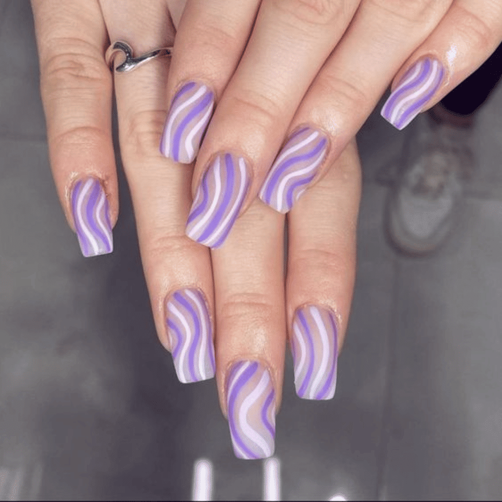 Close-up of hands with manicured nails featuring wavy patterns in shades of purple and white, creating a trendy look.