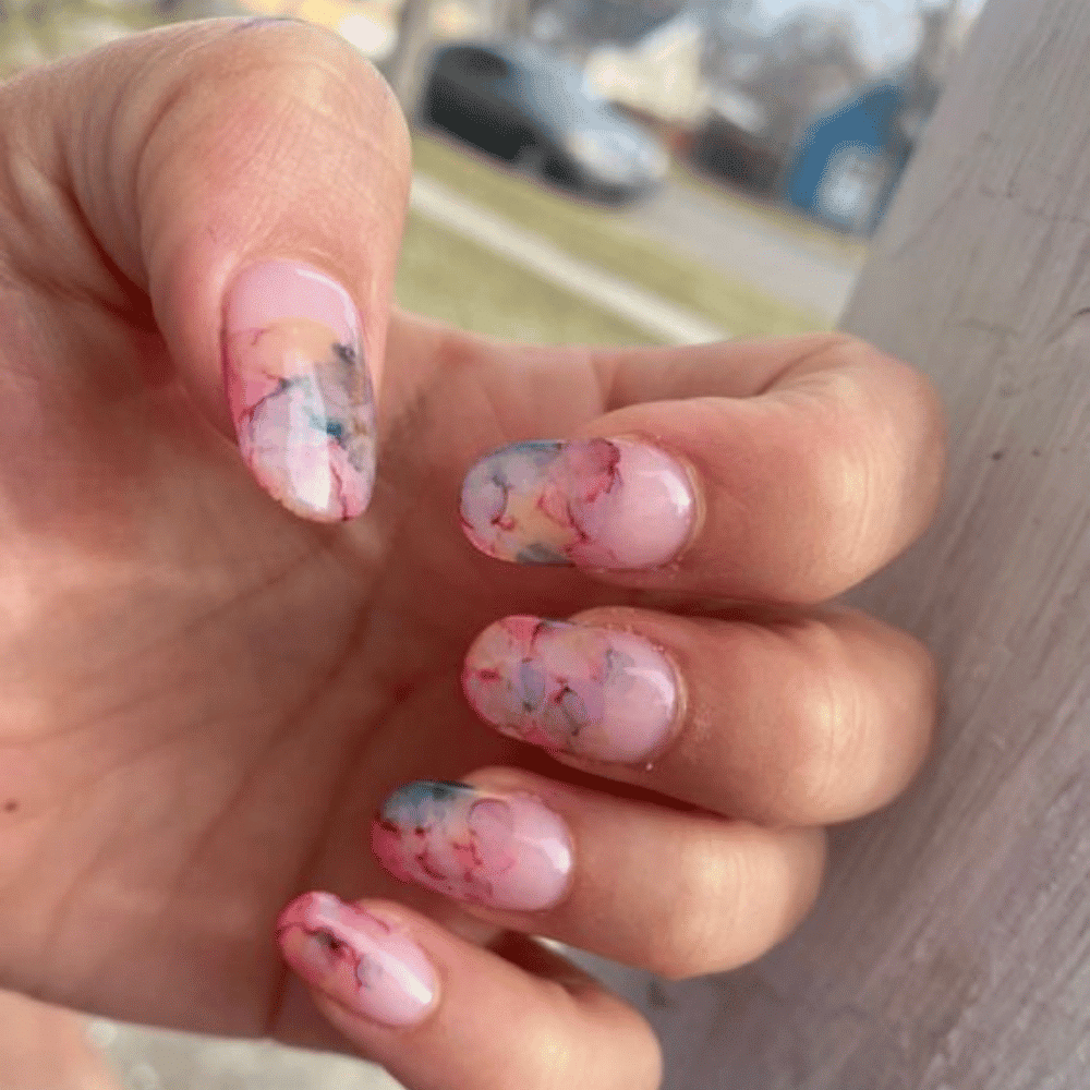 A woman showcasing her vibrant nail designs, featuring an array of colors and intricate patterns on her fingers.