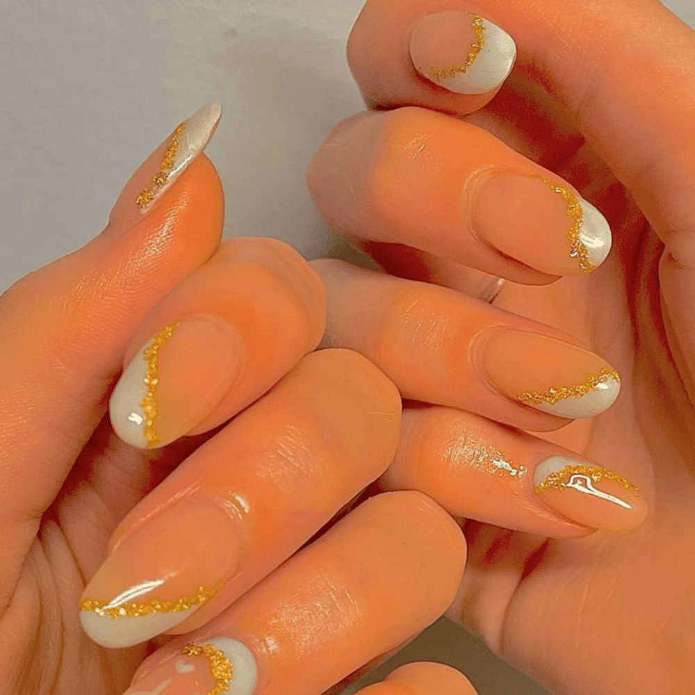 A woman displays her orange and white nails while holding a gold and white manicure set in her hands.