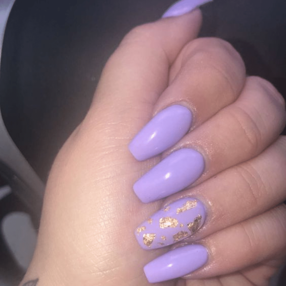 A hand with long, lavender-colored nails, one nail featuring gold foil accents.