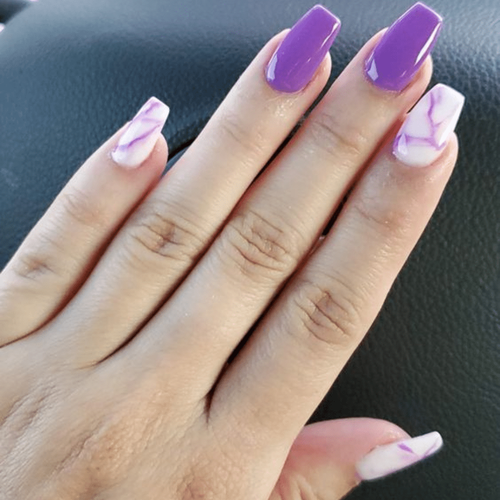 A hand with purple and white marble-patterned acrylic nails on a black background.