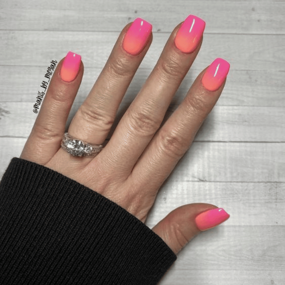 A close-up of a woman's hand showcasing vibrant pink and orange nails, elegantly manicured and well-groomed.