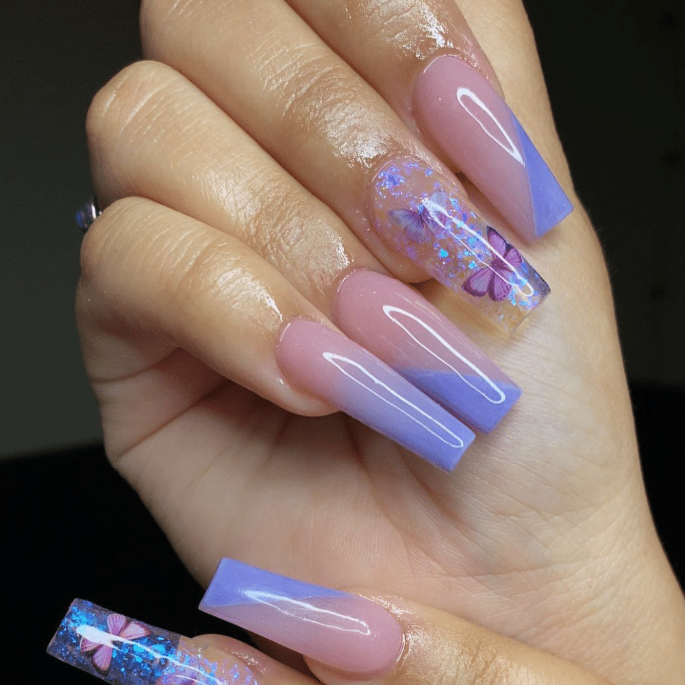 Hand with long, glossy, square-shaped nails featuring pink and purple designs, including butterflies and glitter.