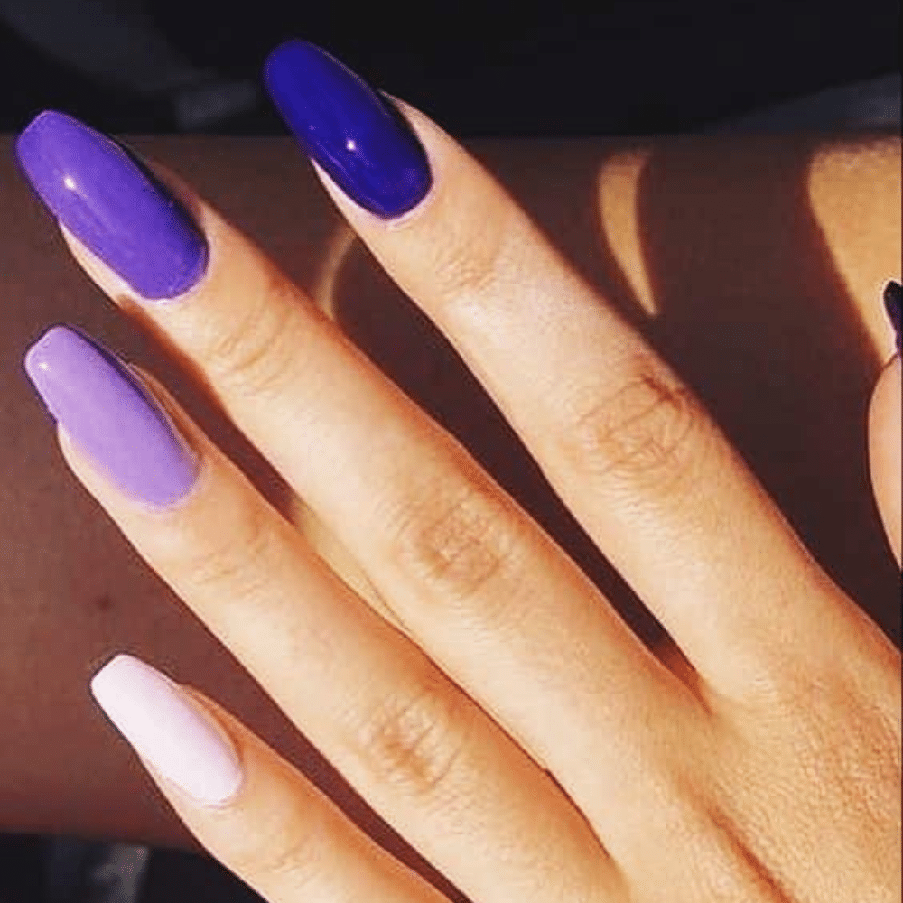 A hand with long, manicured nails painted in various shades of purple and blue, displayed in sunlight.