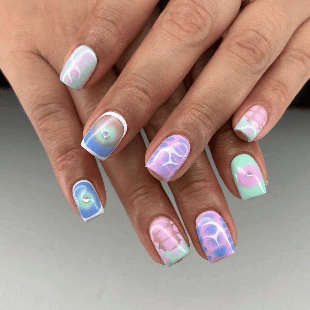 A close-up of a woman's hand showcasing a vibrant and artistic nail design with various colors and patterns.