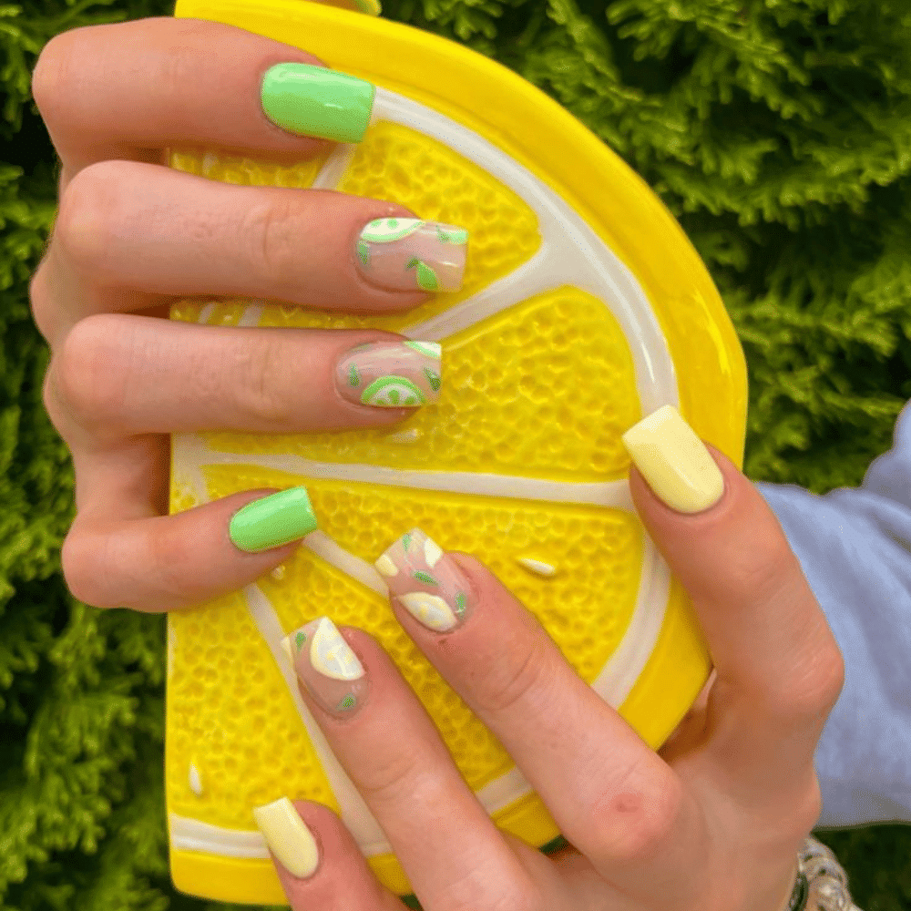 A woman displays a lemon slice, showcasing her vibrant yellow and green manicure.