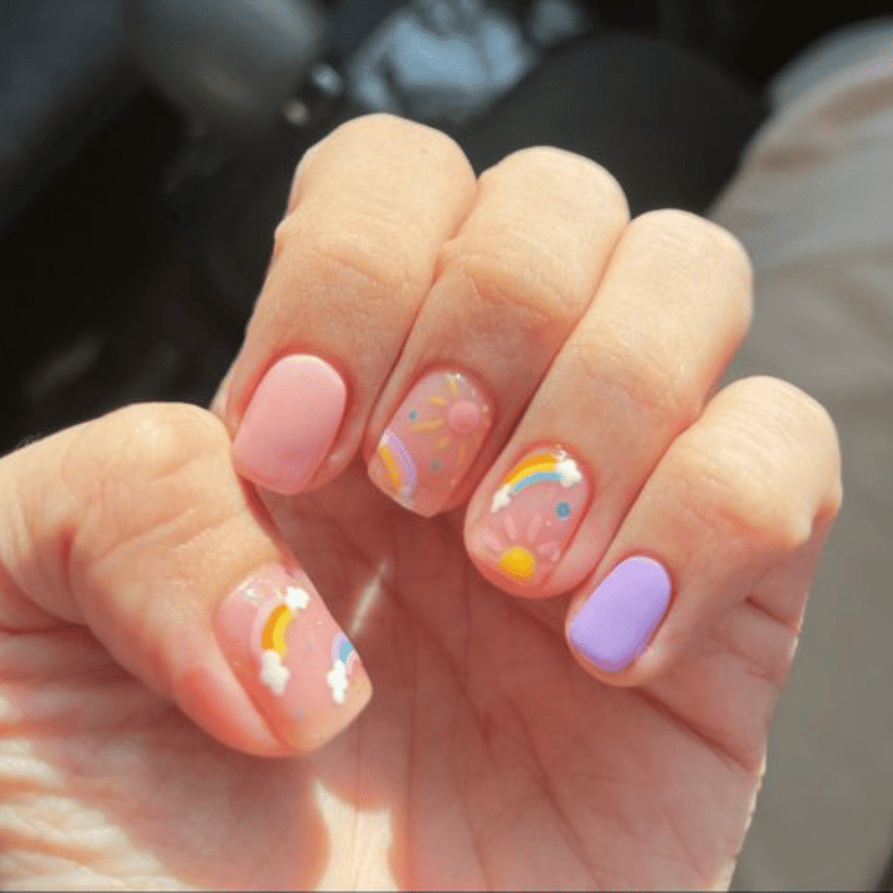 A person displays their manicured nails, adorned with a rainbow design and sparkling stars in the background.