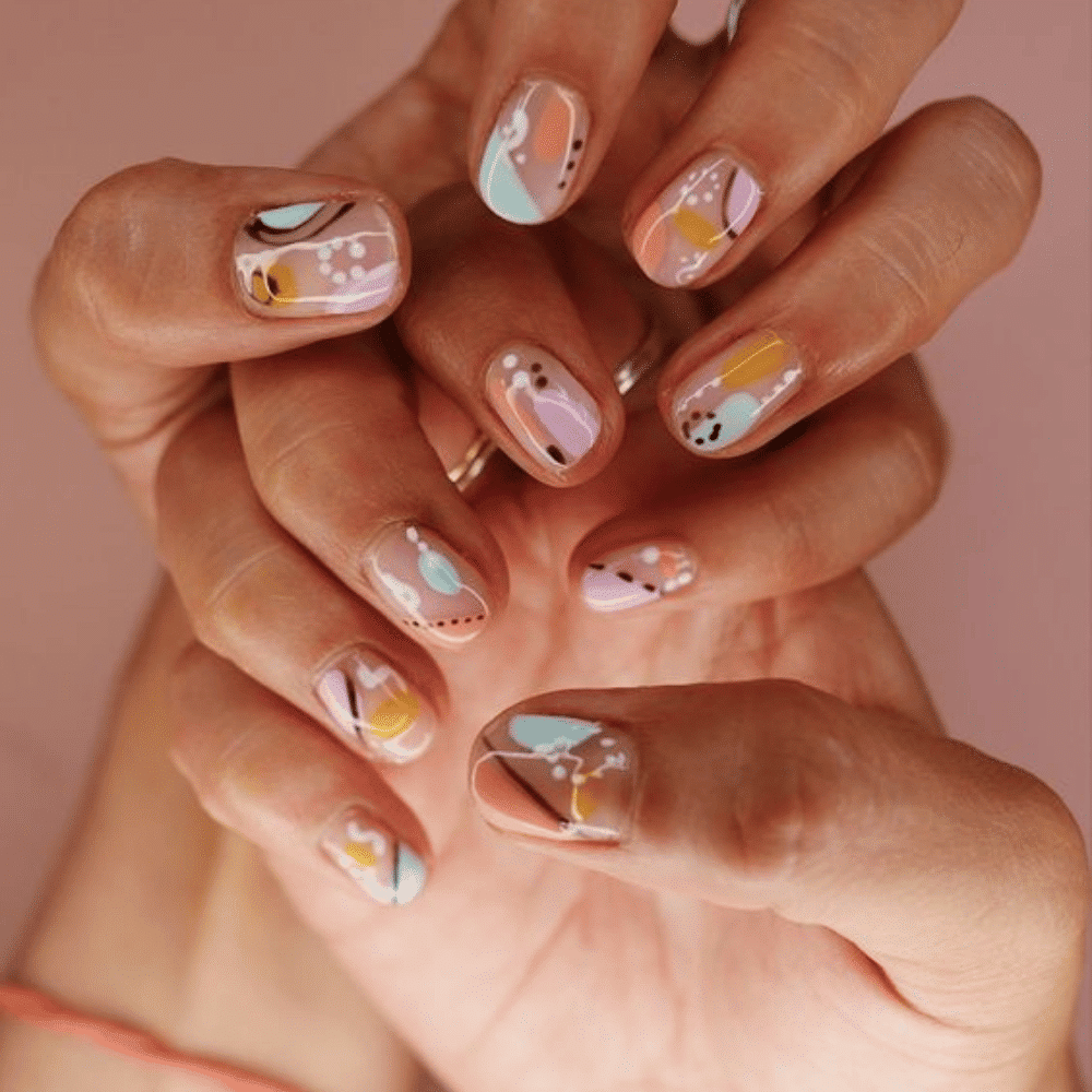 A woman displays her hands with vibrant, artistic nail designs, showcasing a variety of colors and patterns.