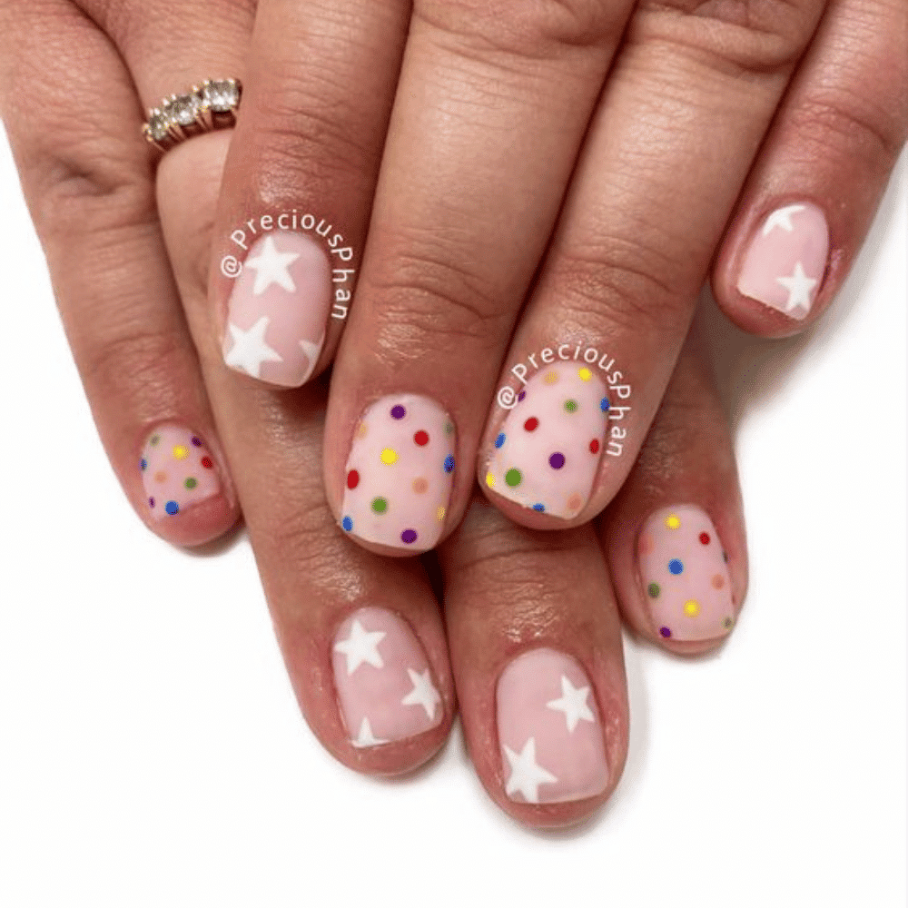 A close-up of a woman's hand showcasing a vibrant nail design adorned with colorful stars.