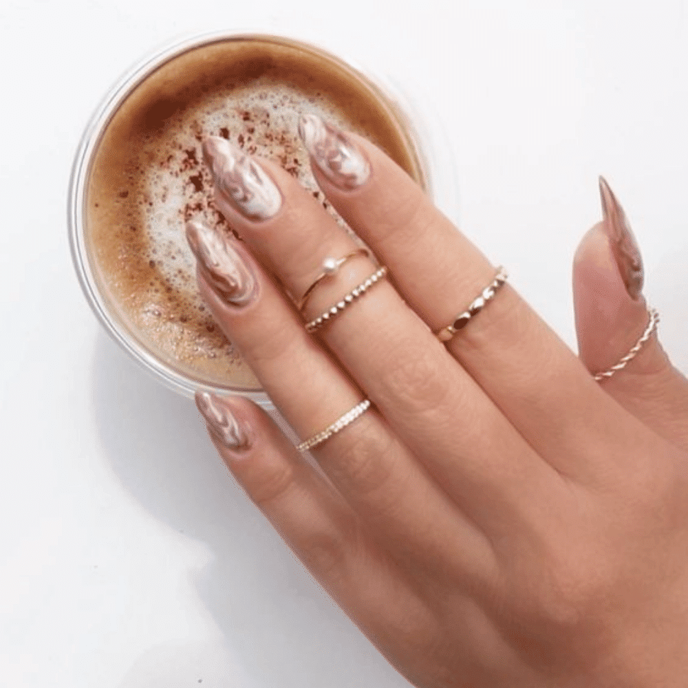 A woman's hand elegantly holds a cup of coffee, showcasing a beautiful ring on her finger.