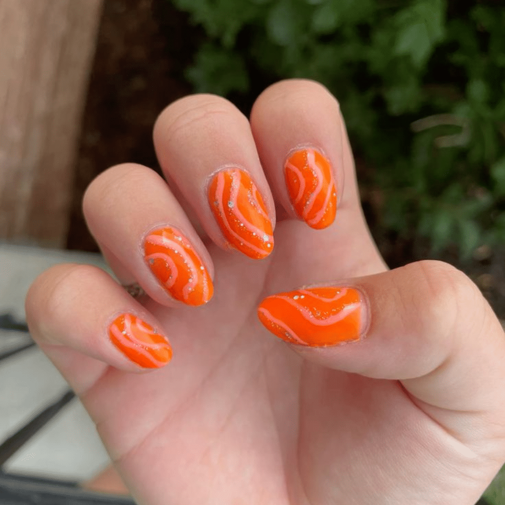 Close up of nails with glittery orange nails having Abstract Orange Swirls and Dots