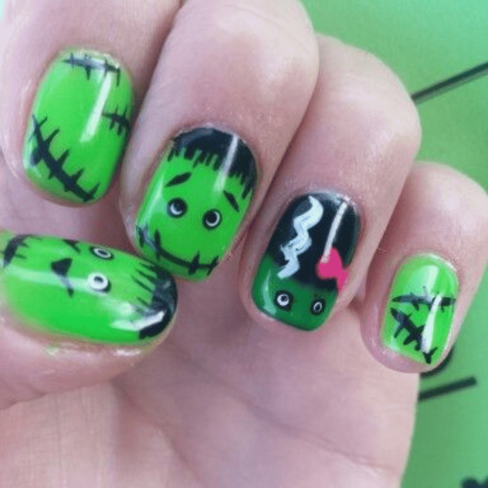 Close-up of nails painted with Halloween-themed green, black, and white designs resembling Frankenstein’s monster and his bride.