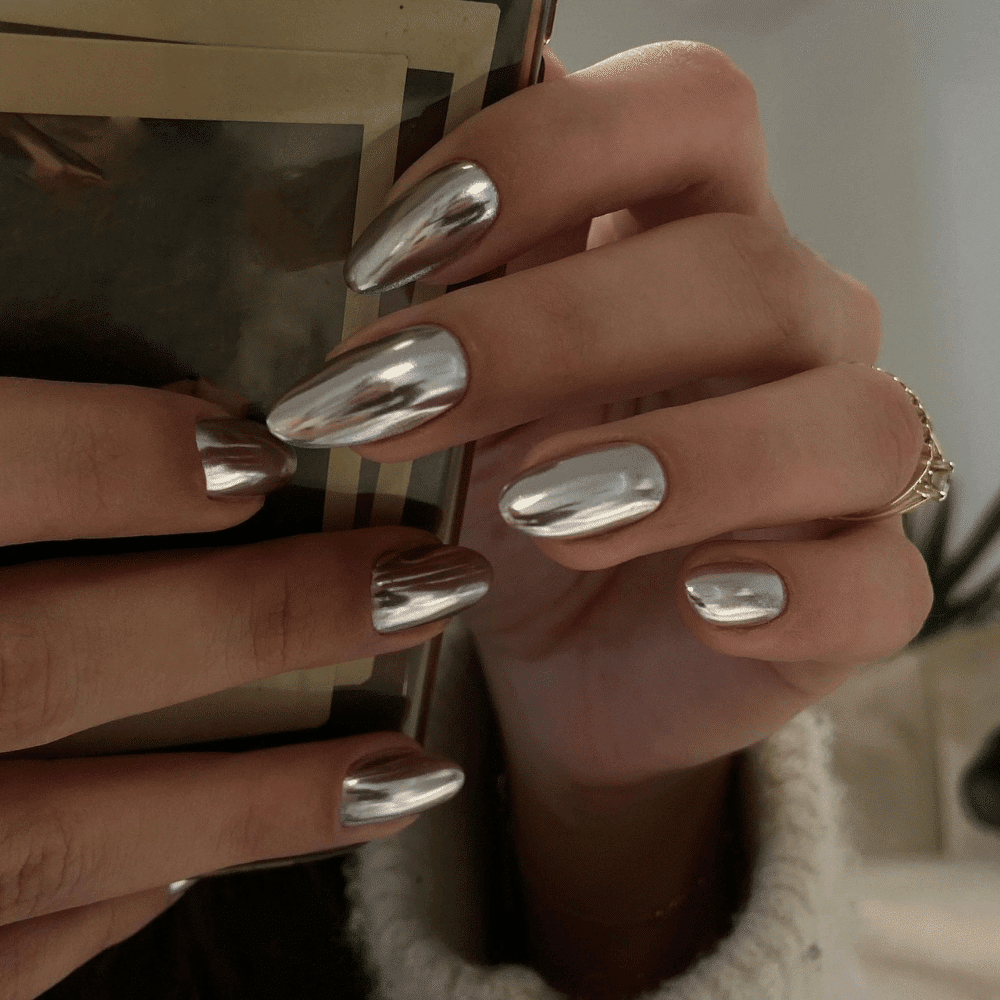 A woman with shiny silver nails is holding an open book, showcasing her elegant style and love for reading.