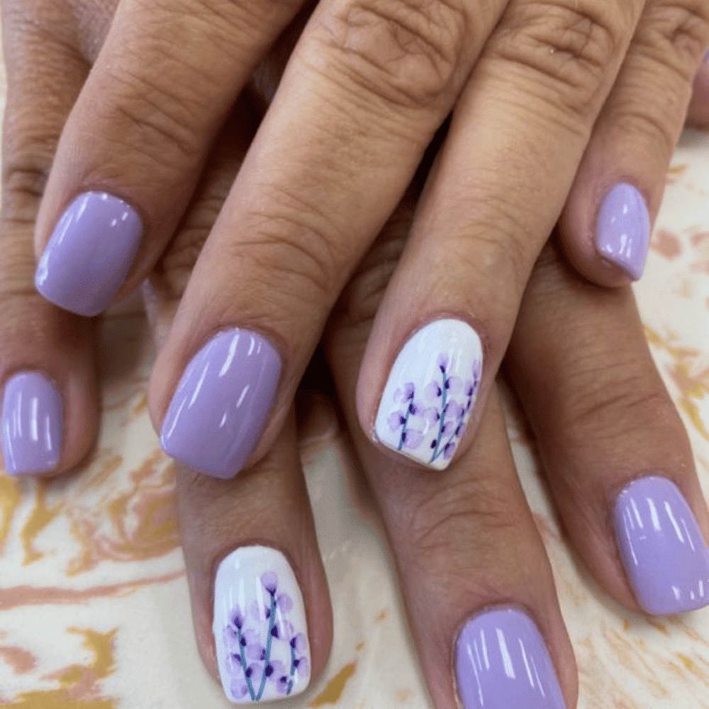 Close-up of hands with light purple nails and ring fingers featuring a floral design with purple flowers.