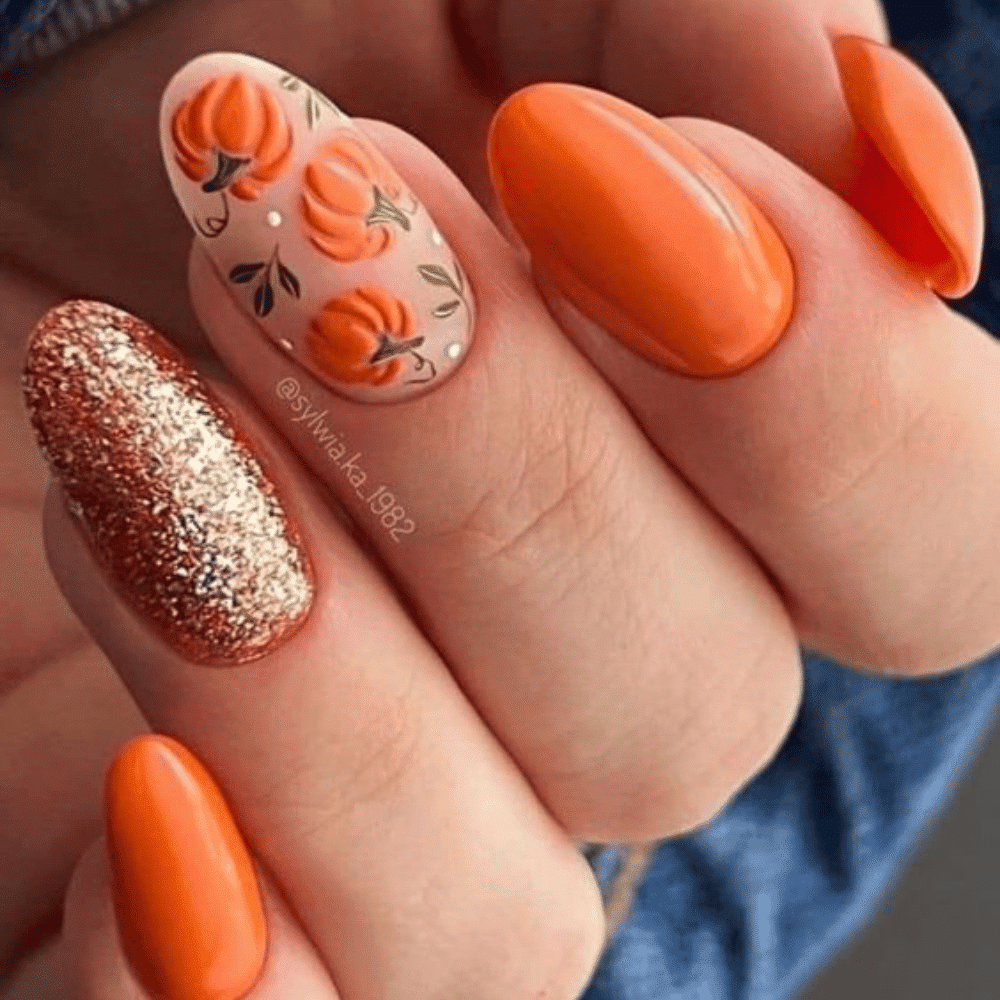 Hand with orange Halloween-themed nails, featuring pumpkins, glitter, and solid color designs.