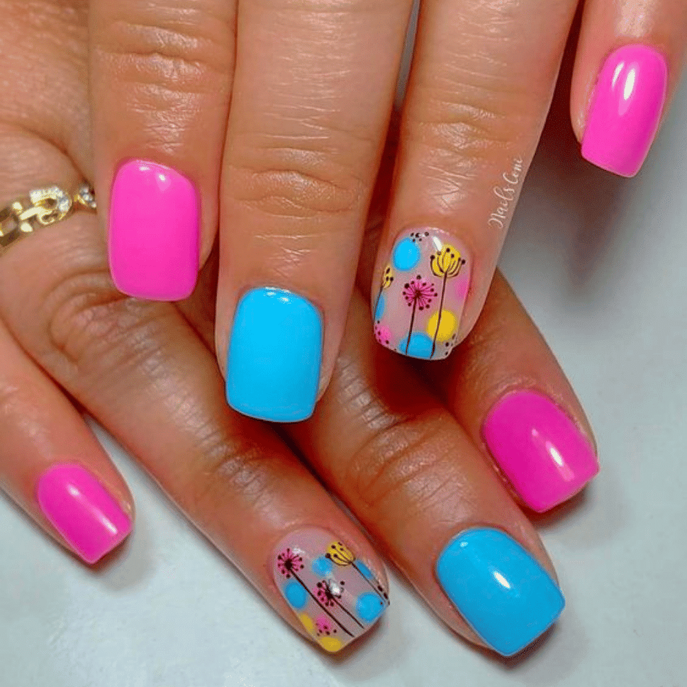 A close-up of a woman's hand showcasing pink and blue floral nail art on her manicured nails.