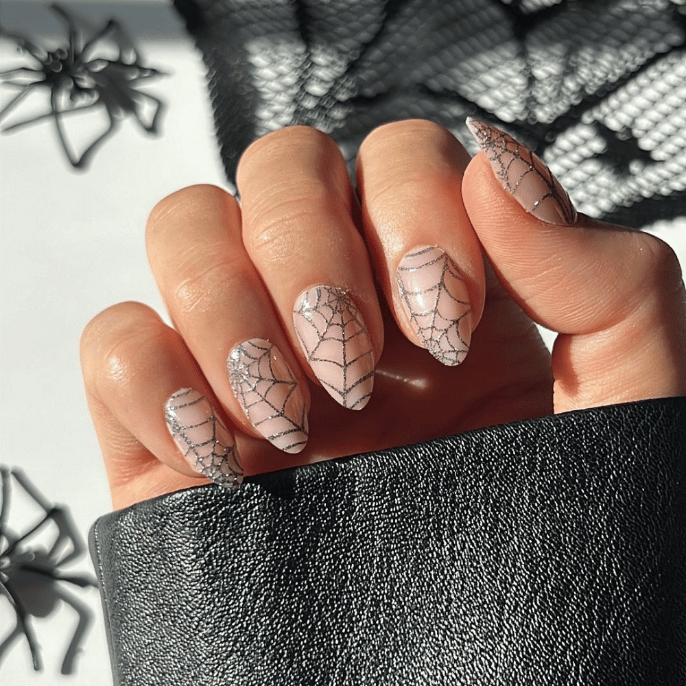 Hand with light pink nails featuring intricate black spider web designs, holding black textured material.