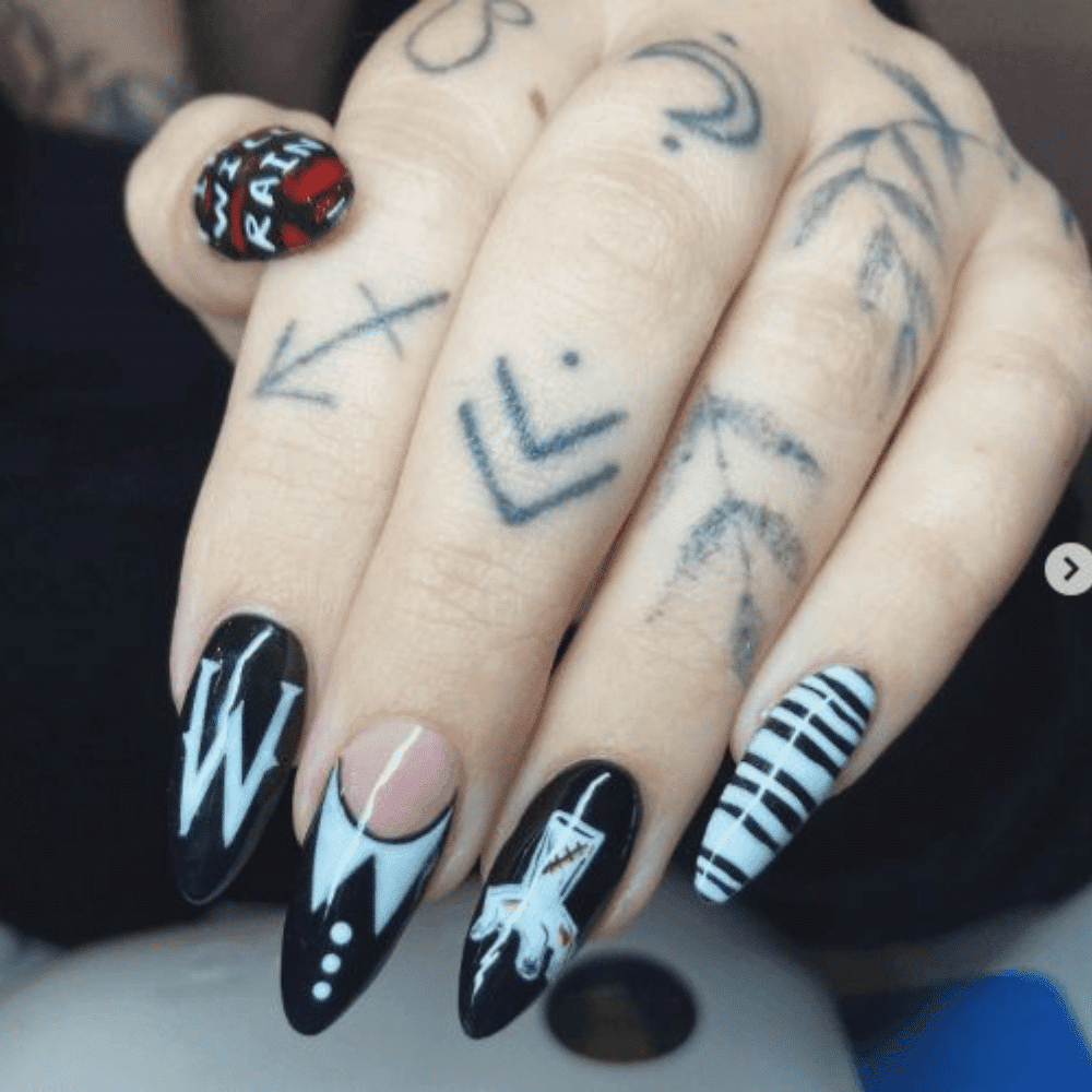 Close-up of a hand with tattoos and intricate nail art featuring varied black and white designs on each nail.