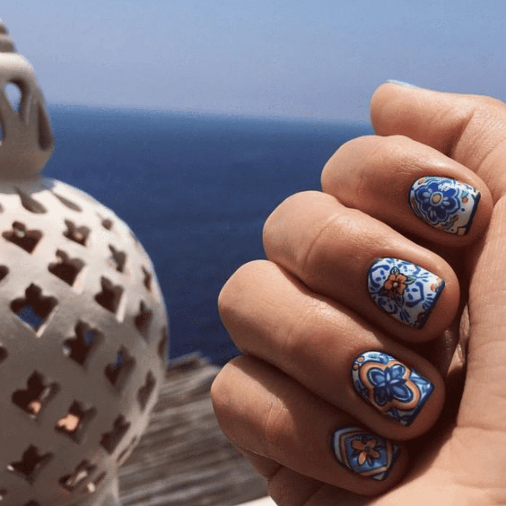 A person showcasing their blue and white nail art, highlighting intricate designs on their manicured nails.