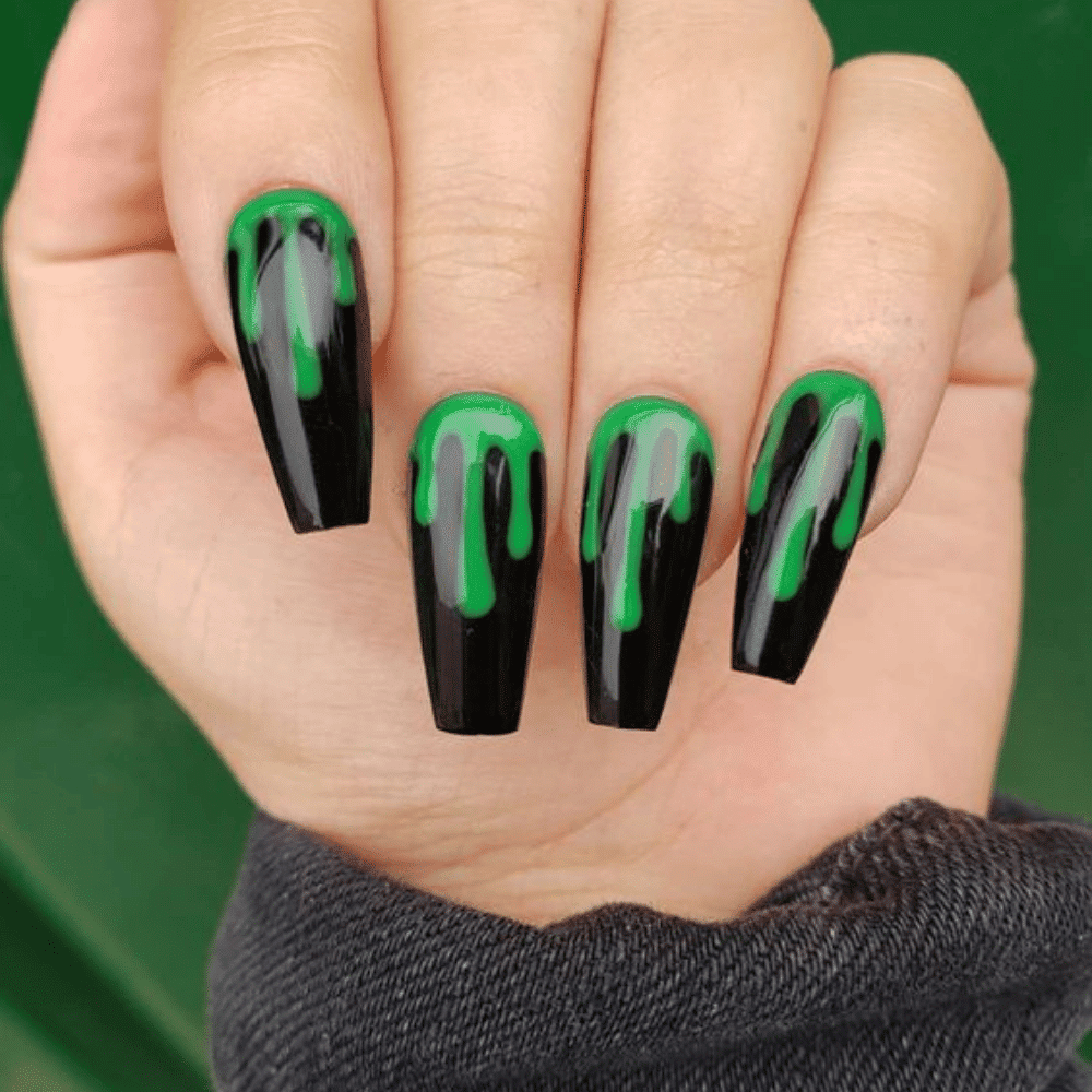 Close-up of a hand with long, coffin-shaped nails painted black with green dripping effect from cuticle to tip.