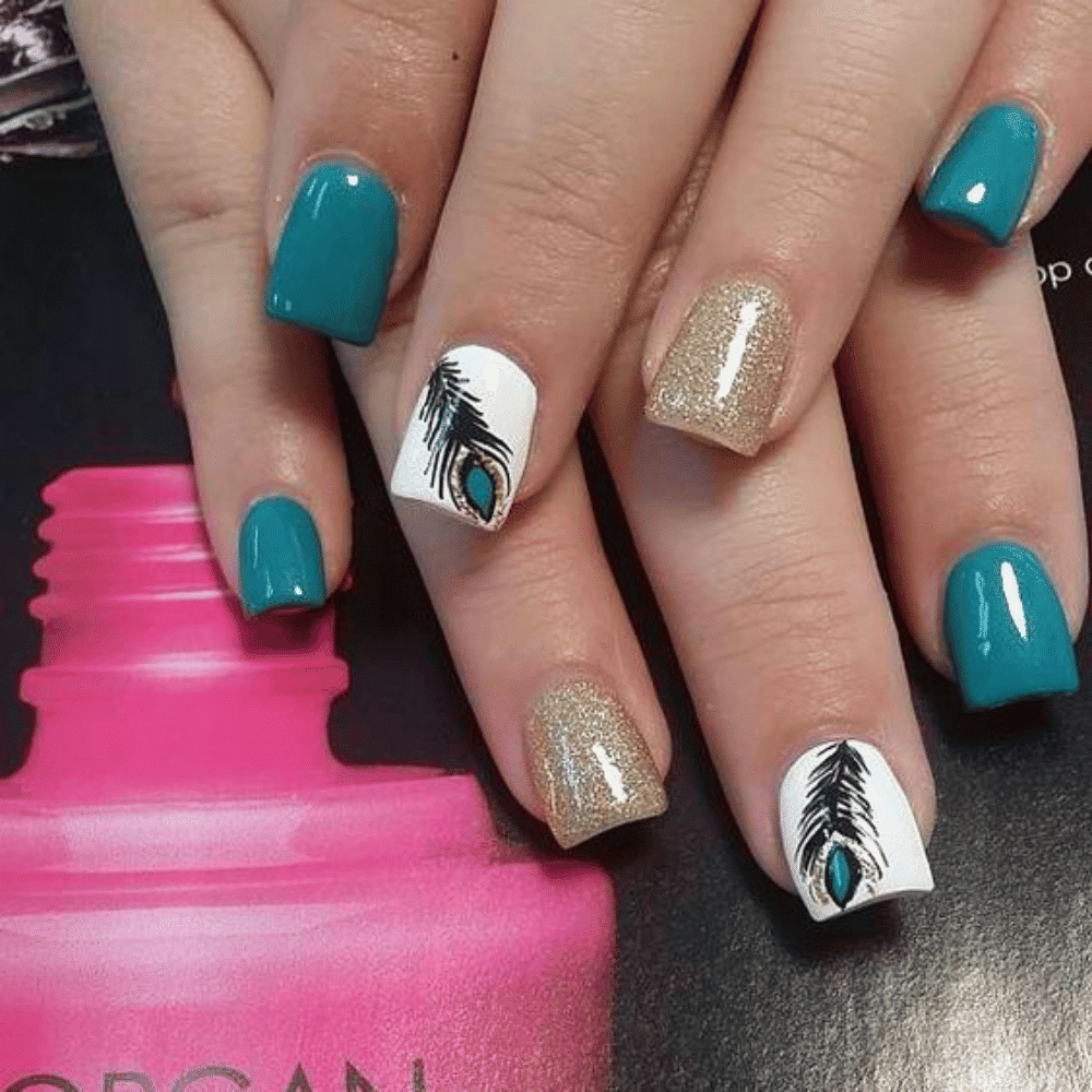 A close-up of a woman's hand showcasing a blue and gold manicure featuring an elegant feather design.