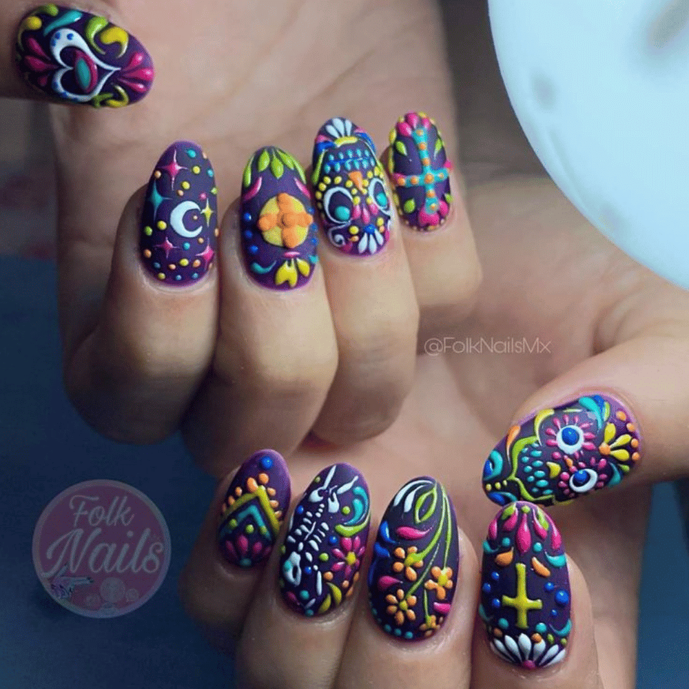 Hands with nails decorated in traditional Mexican folk art, featuring colorful designs like skeletons, flowers, and moons.