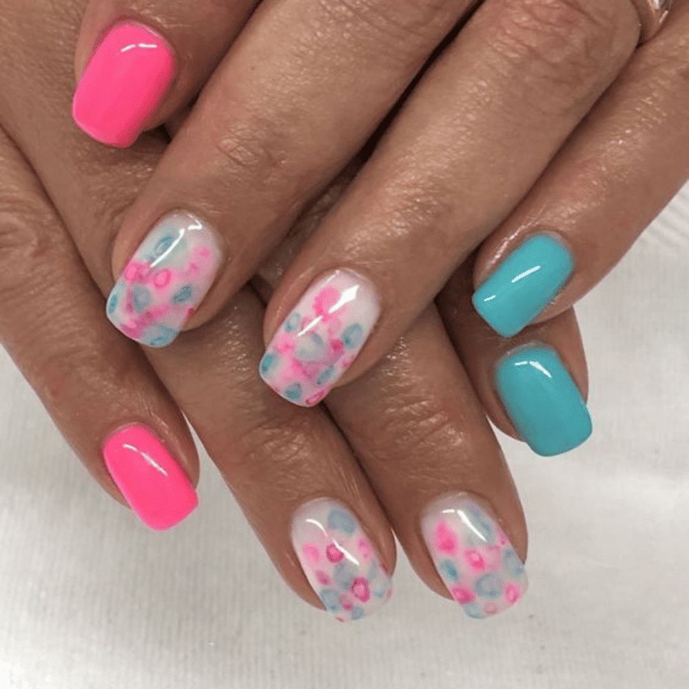 A close-up of a woman's hands showcasing pink and blue nails adorned with a delicate flower design.