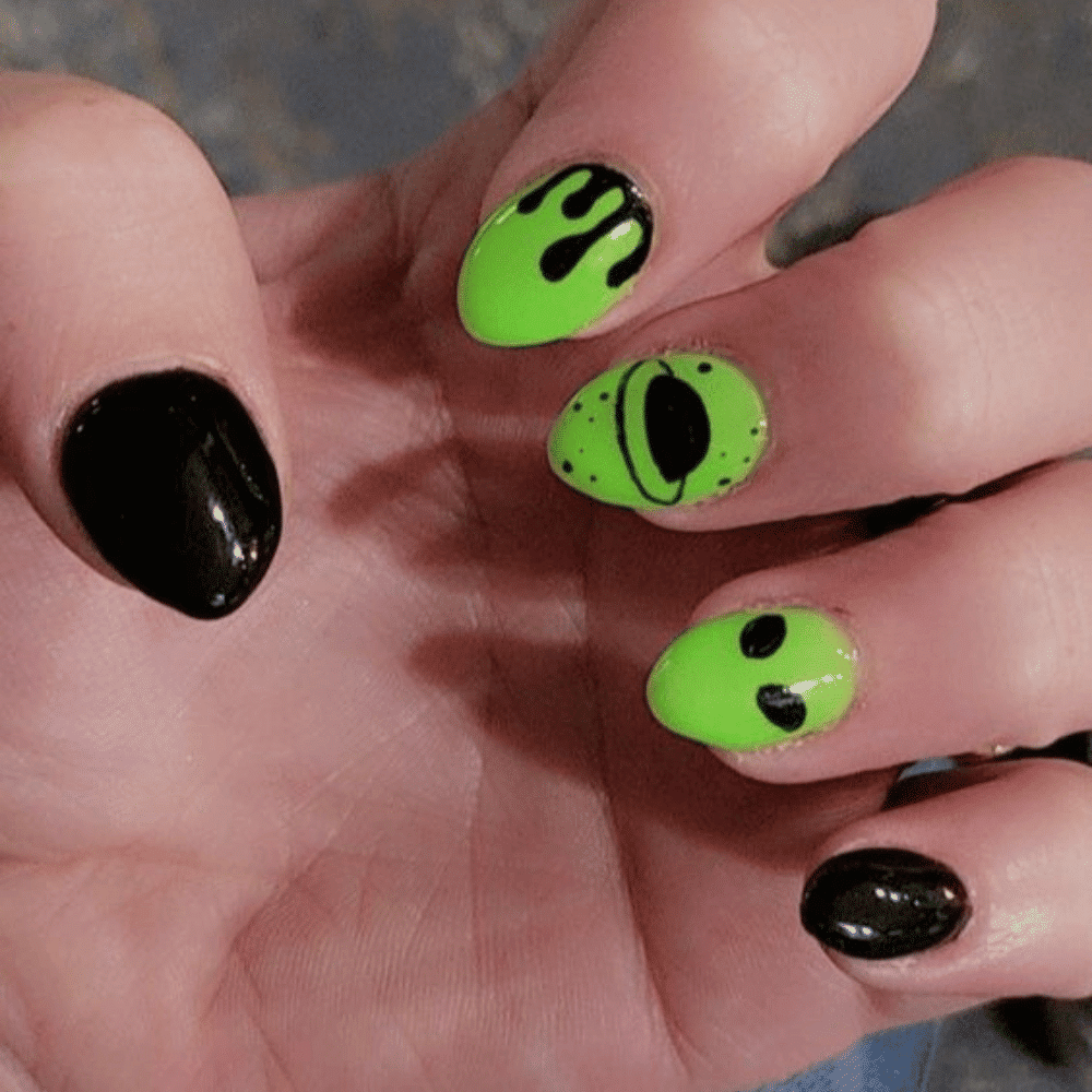 Close-up of a hand with neon green and black nail art, featuring a dripping effect, a planet, and an alien face.