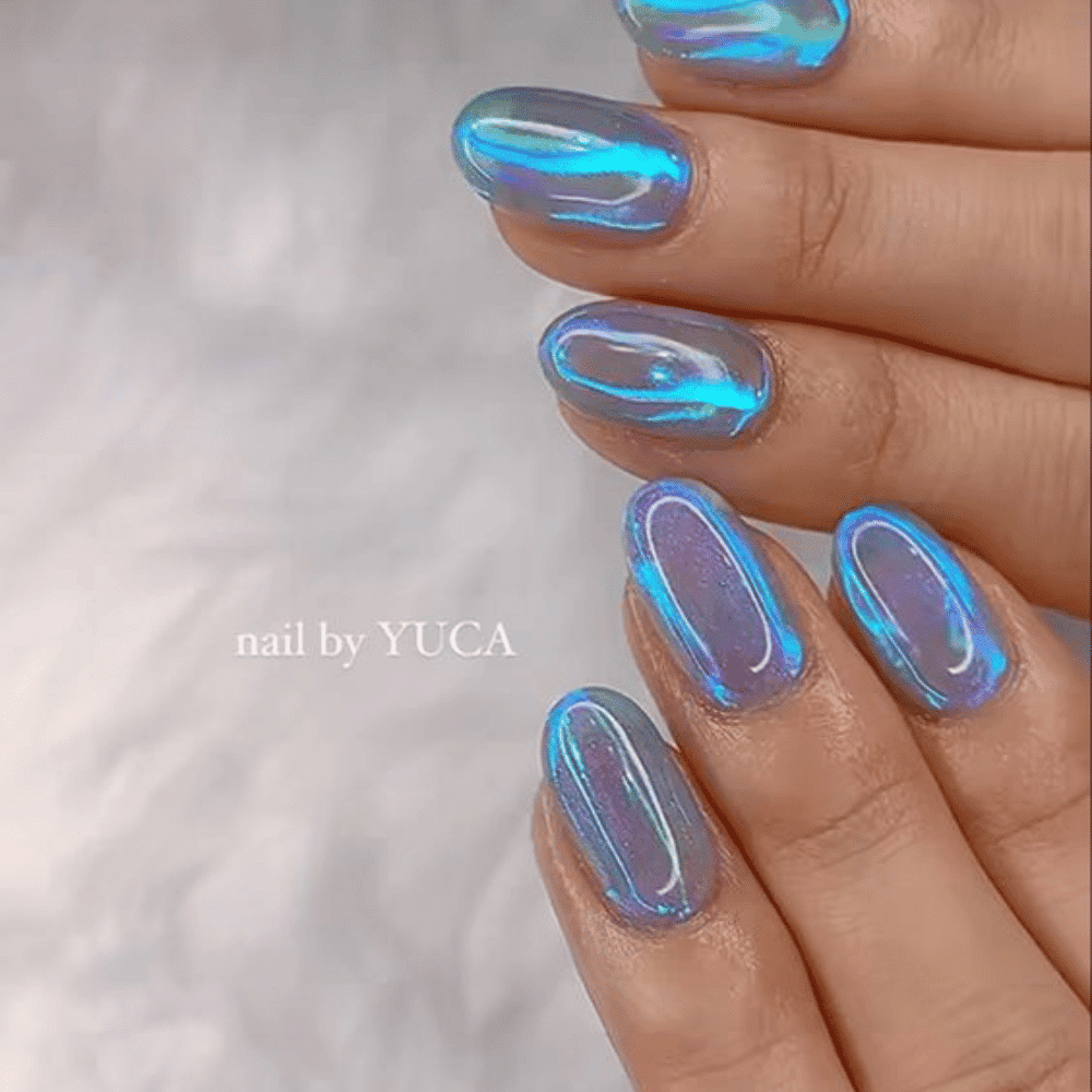 A close-up of a person's hands showcasing blue and holographic nail polish on their nails, reflecting light beautifully.