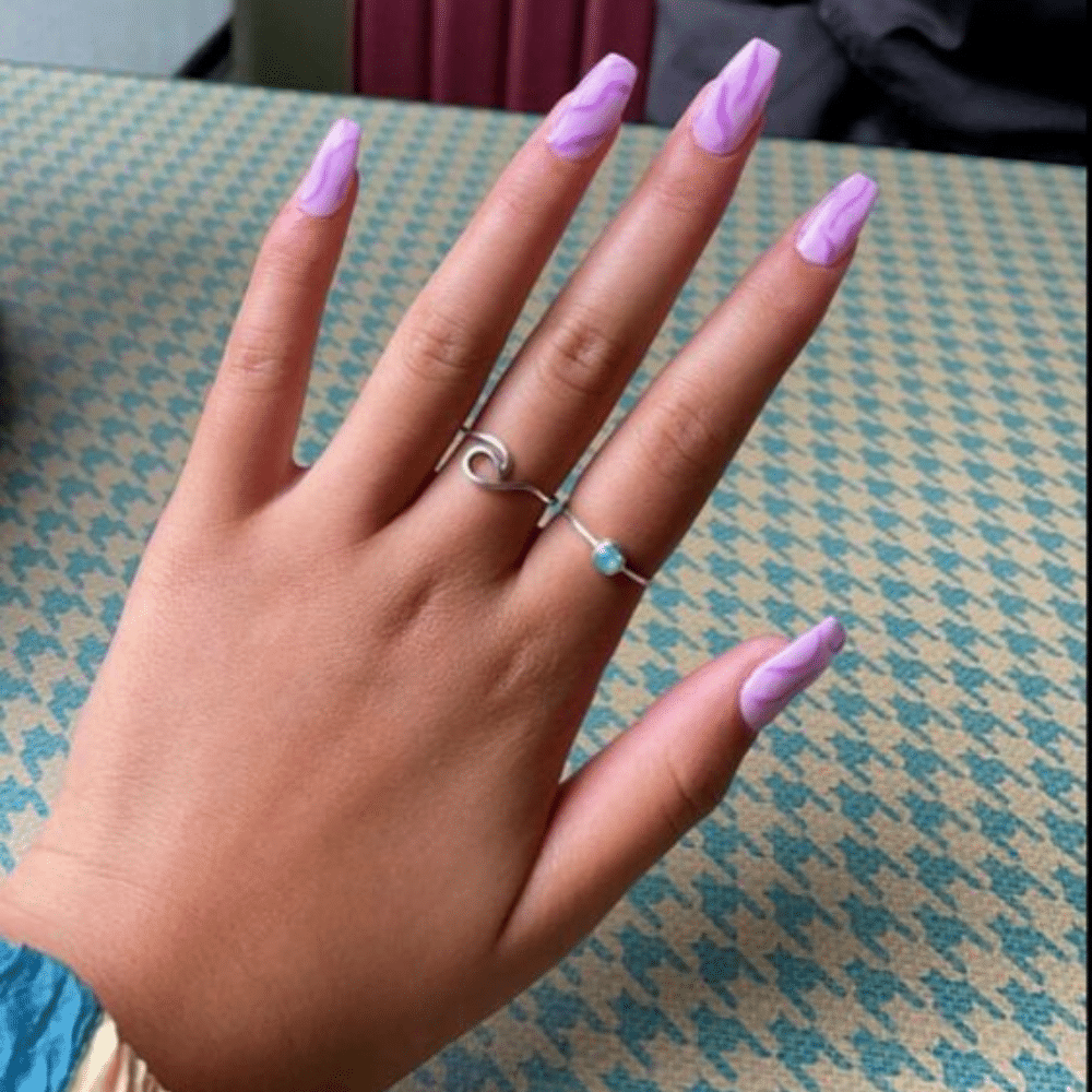 A hand with purple marble nails and two silver rings on a patterned surface.