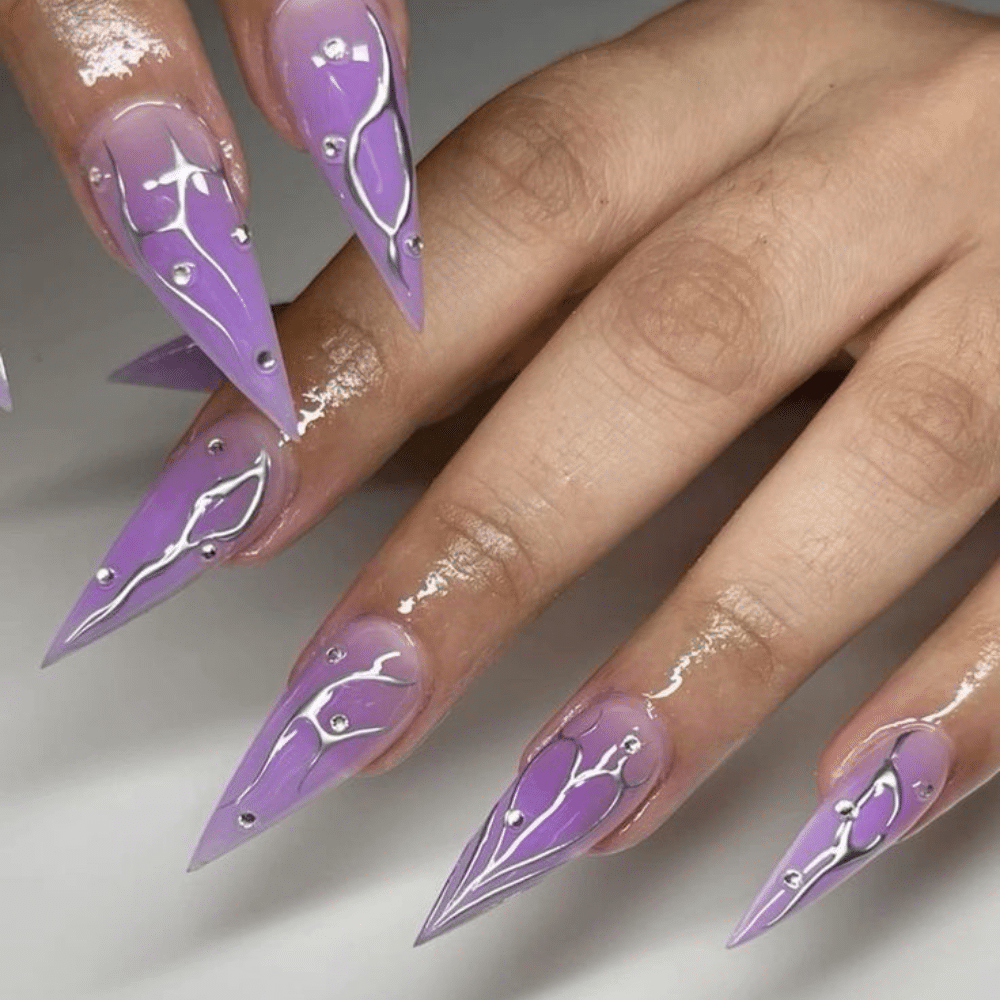 Close-up of hands with long, pointed, purple nails featuring silver lines and small rhinestones.