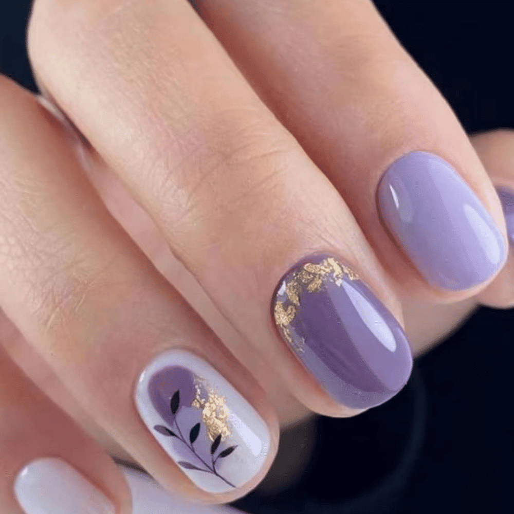 A close-up of a woman's hand showcasing purple and white nails adorned with elegant gold leaf accents.