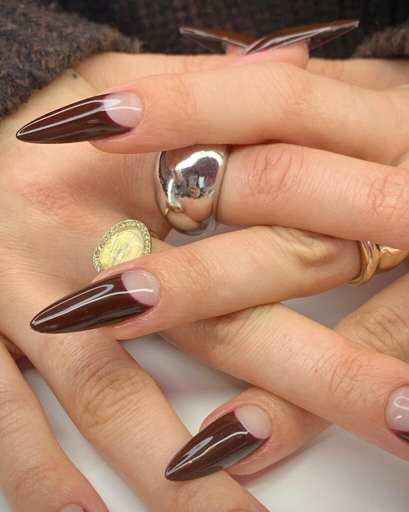 Close-up of a hand with long, pointed nails, featuring glossy maroon and metallic silver polish.