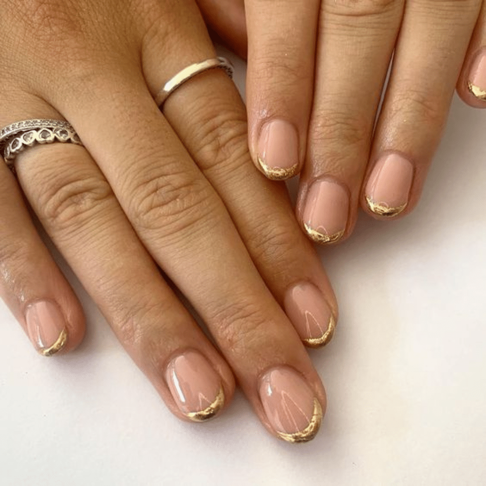 Close-up of a hand with white French tip gold and silver lined nail