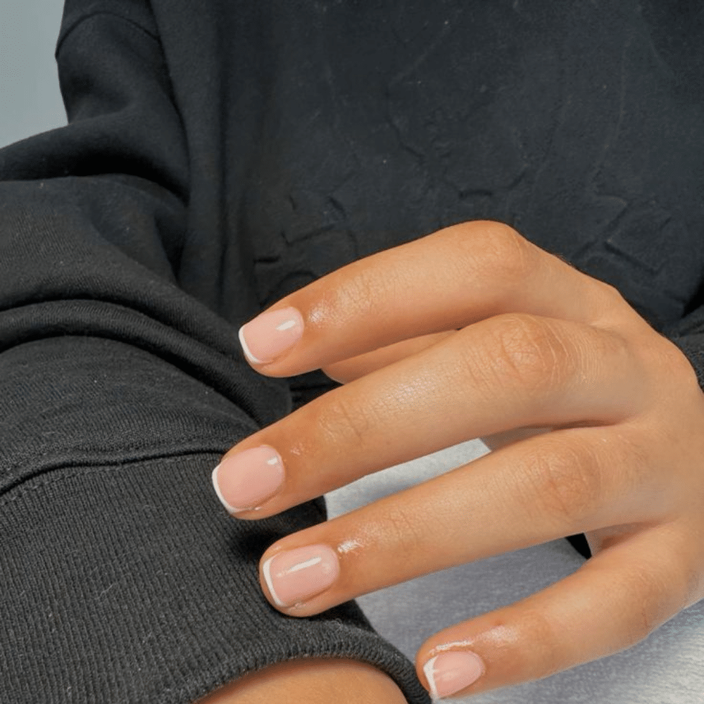 Close-up of a hand with manicured white french tip nails resting on a black fabric surface.