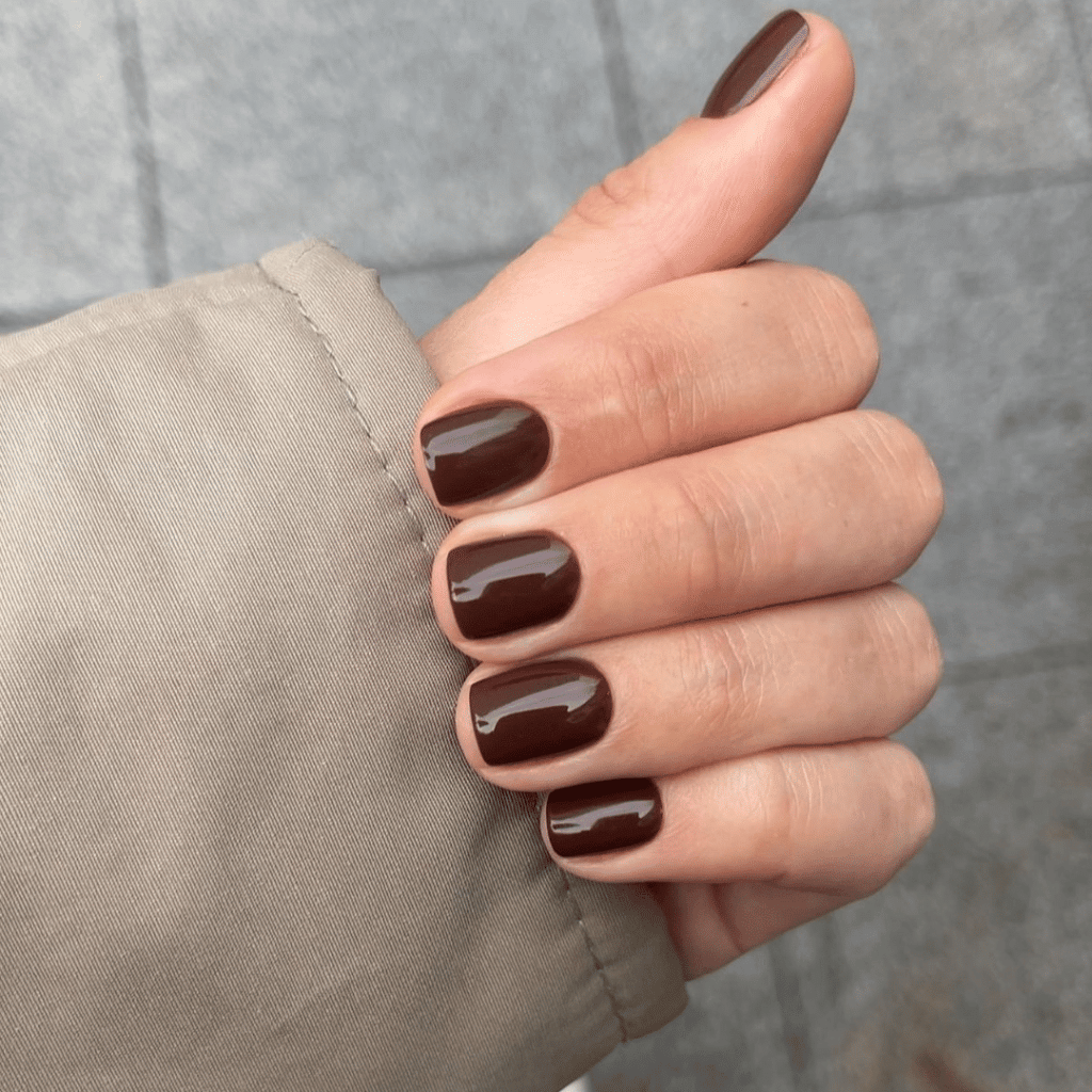 A close-up of a hand with brown polished nails resting on a beige fabric surface.